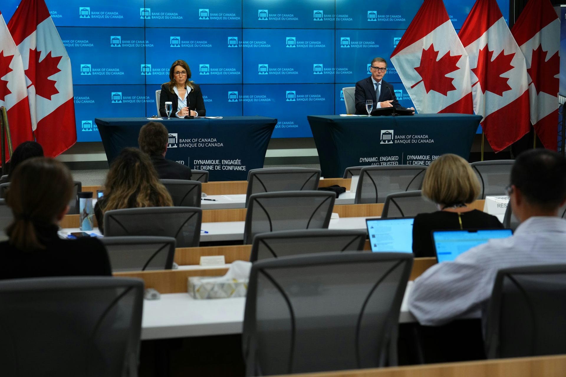 A man and a woman give a press conference to an audience of people who are taking notes