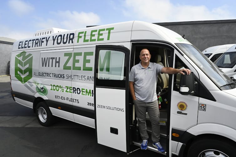 A man in a white shuttle bus painted with branding and '100% Zero Emission.'