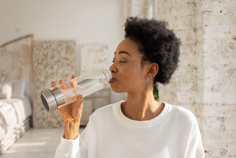 person drinks from fancy glass water bottle