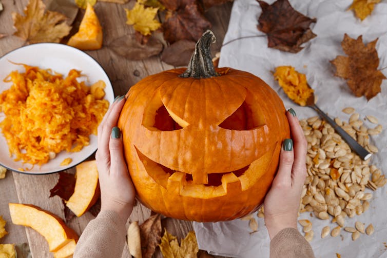 A person holds a carved Halloween pumpkin in their hands.