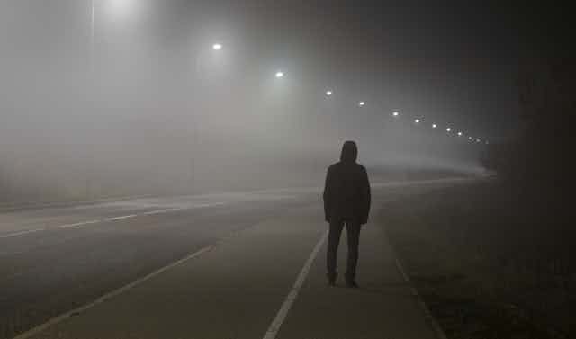 Una persona de espaldas en una calle vacía iluminada por farolas.