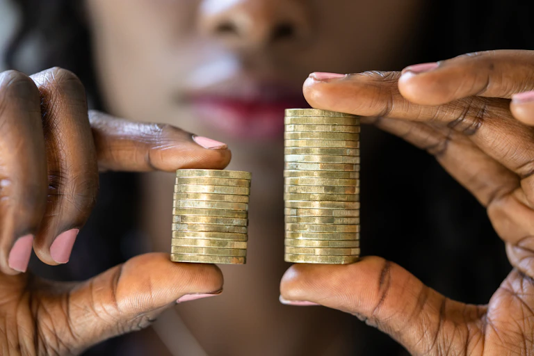 Women comparing two stacks of coins, one larger than the other.