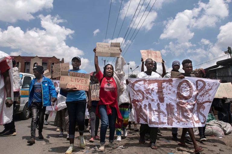 A group of men and women waving homemade placards written 'Stop killings' and 'Our lives matter' while walking along a road.