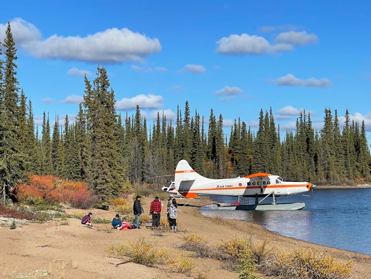 A sea plane on the lake near a forested coast with a few people around.