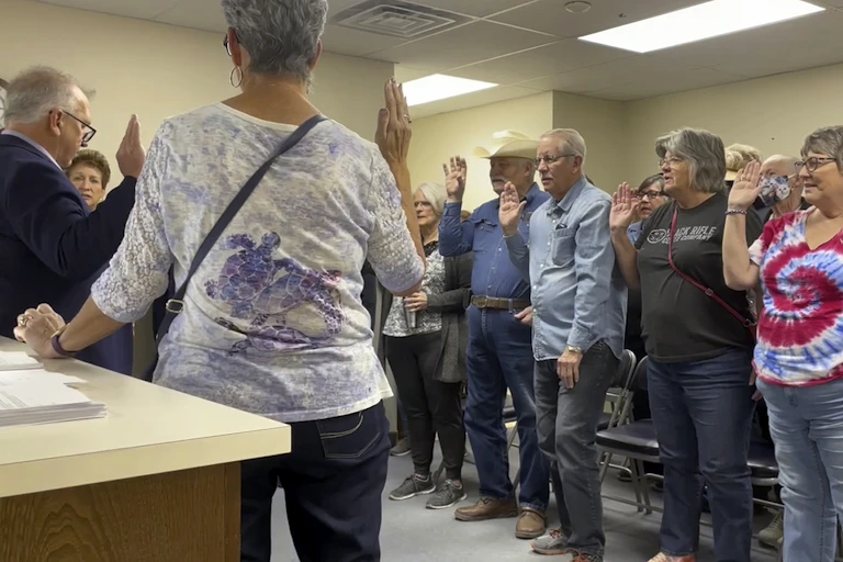 A group of people stand together in a room, all raising their right hands