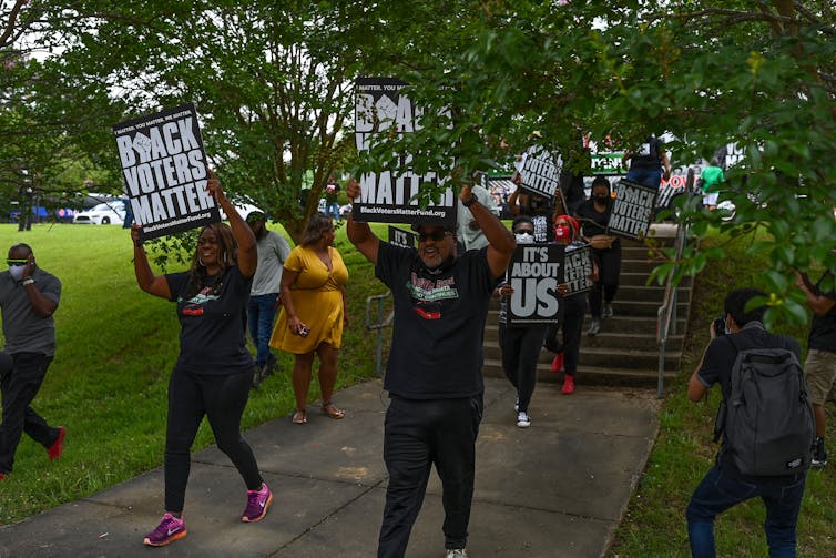 Scores of black demonstrators holding posters march to support black voting rights.