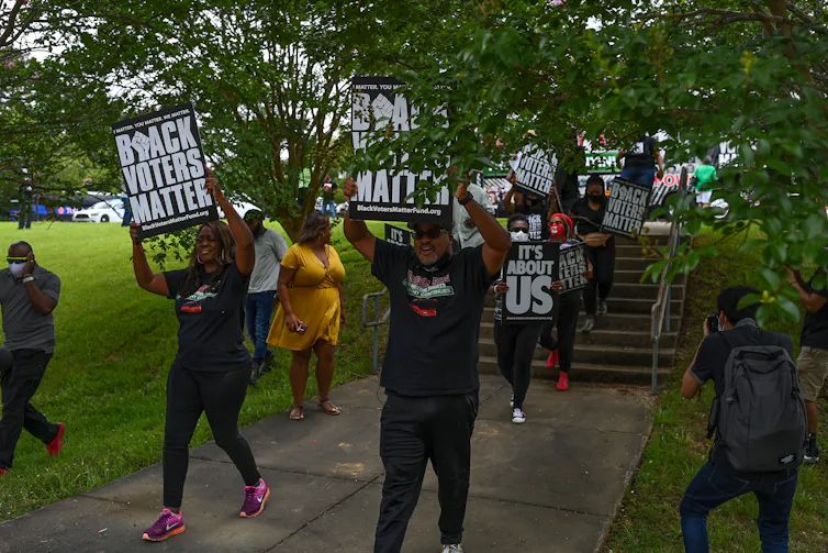 Scores of black demonstrators holding posters march to support black voting rights.