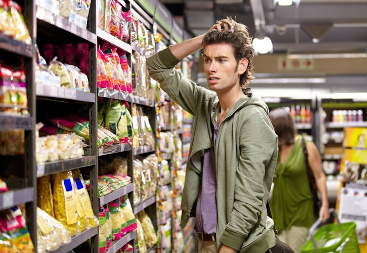 A confused man looking at products on a grocery store shelf.