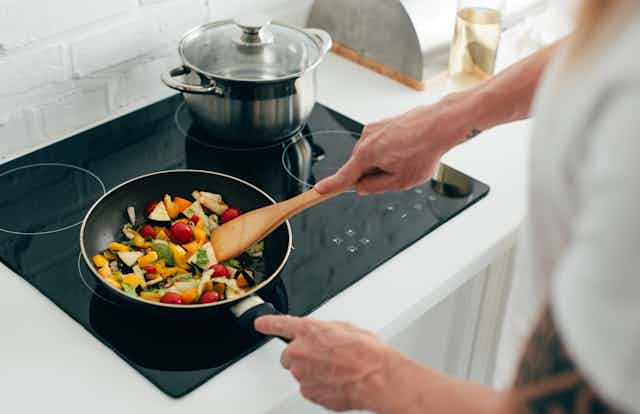 A person cooking vegetables in a pan on an electric stove top.