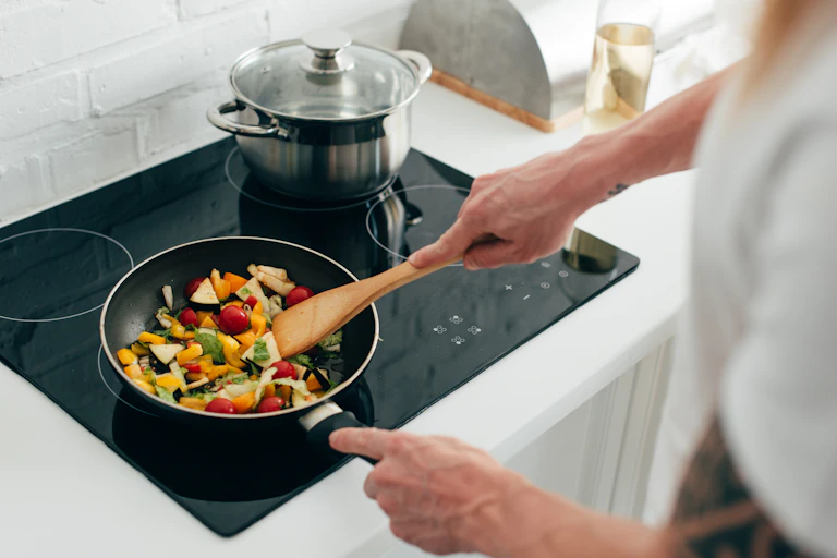 A person cooking vegetables in a pan on an electric stove top.