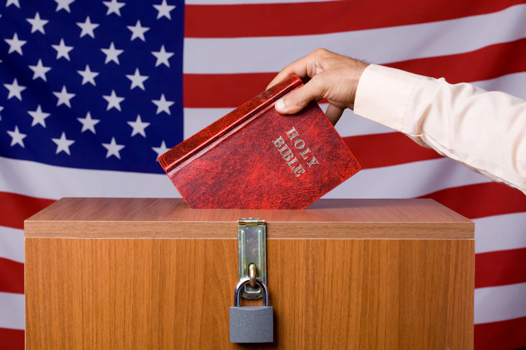 A hand puts a Bible into a locked box in front of a U.S. flag.