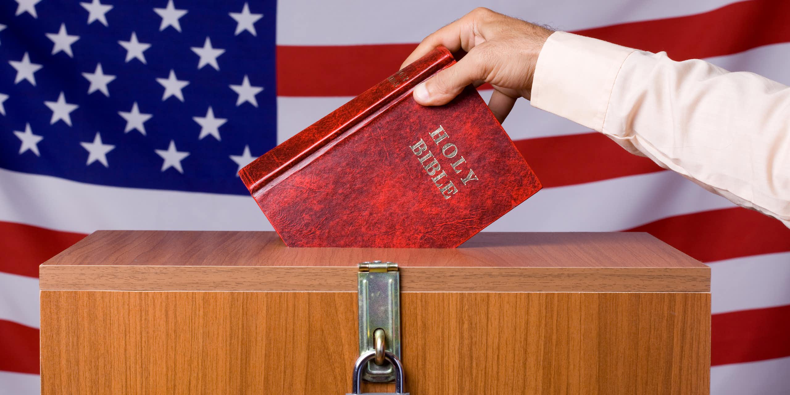 A hand puts a Bible into a locked box in front of a U.S. flag.