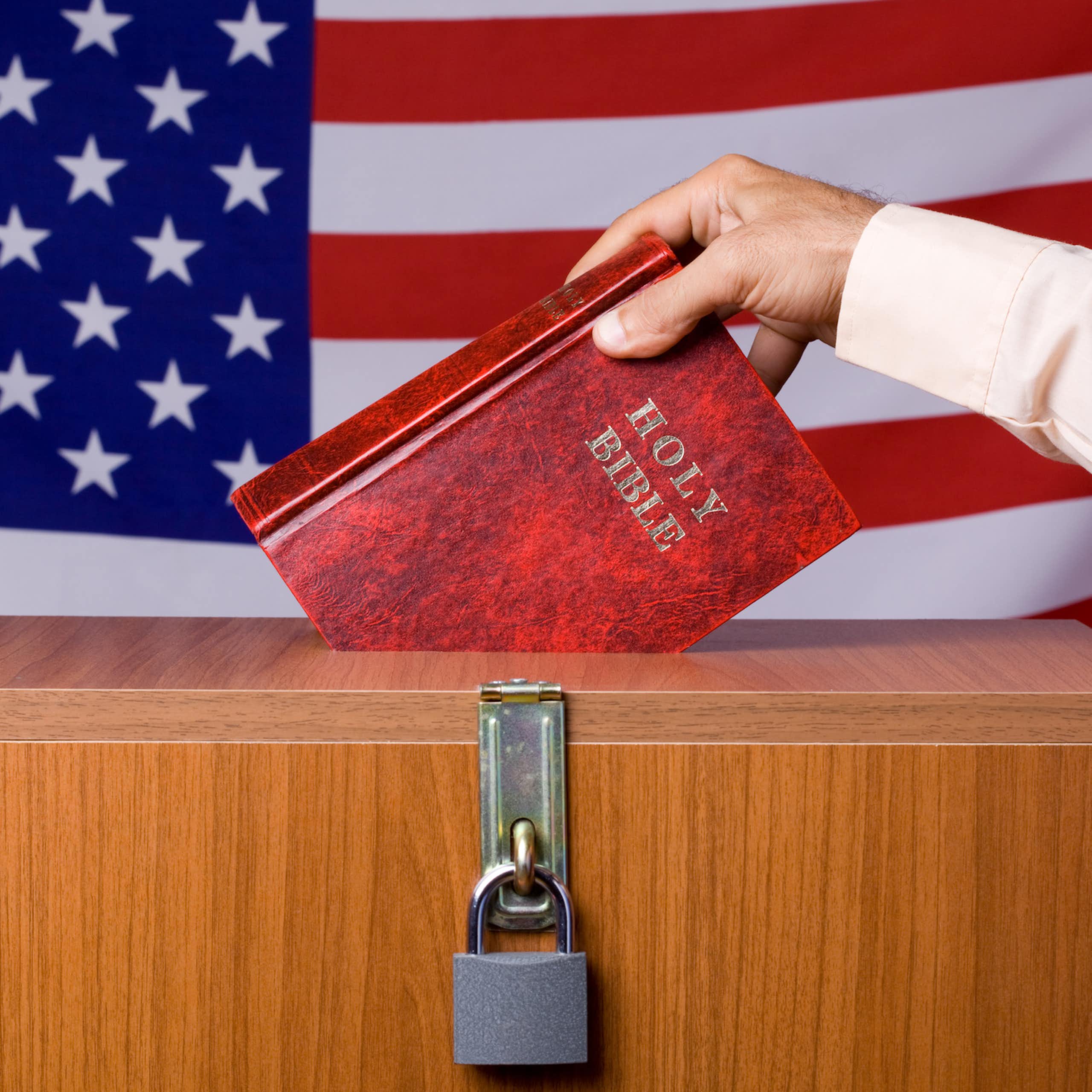 A hand puts a Bible into a locked box in front of a U.S. flag.