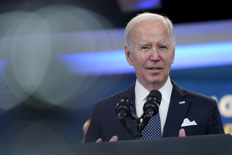 an elderly white man with gray hair and a suit stands behind a lectern