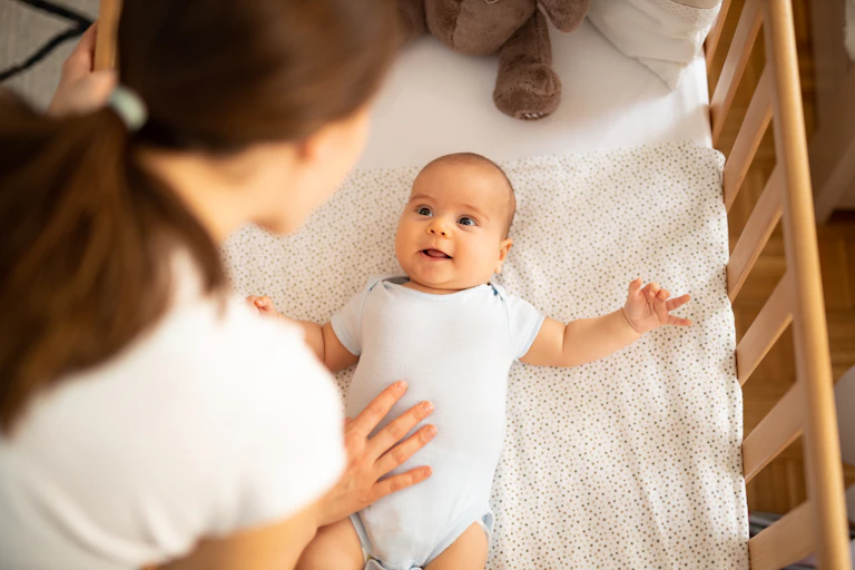 A mother puts her infant child to bed in a crib.