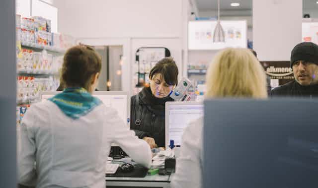 Two customers are served at a pharmacy counter