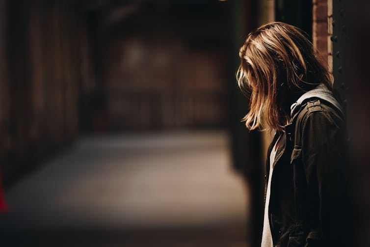 Woman leans against a building at night, her head dipped