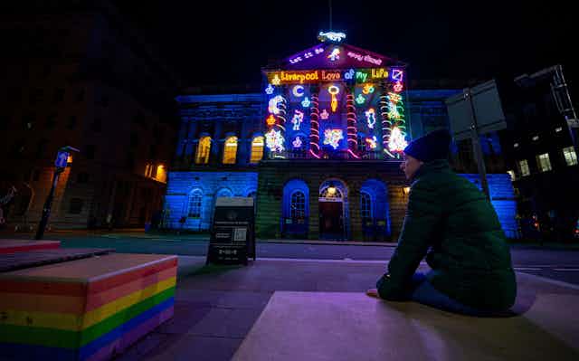 Woman sitting at night in front of building with multicoloured light display