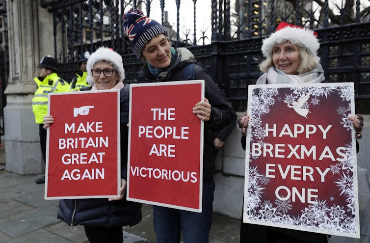 Three people hold pro-Brexit signs, two in Santa hats. One side reads Make Britain Great Again.