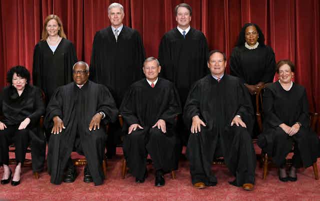 Five men and four women are dressed in black robes are seen posing for a group portrait.