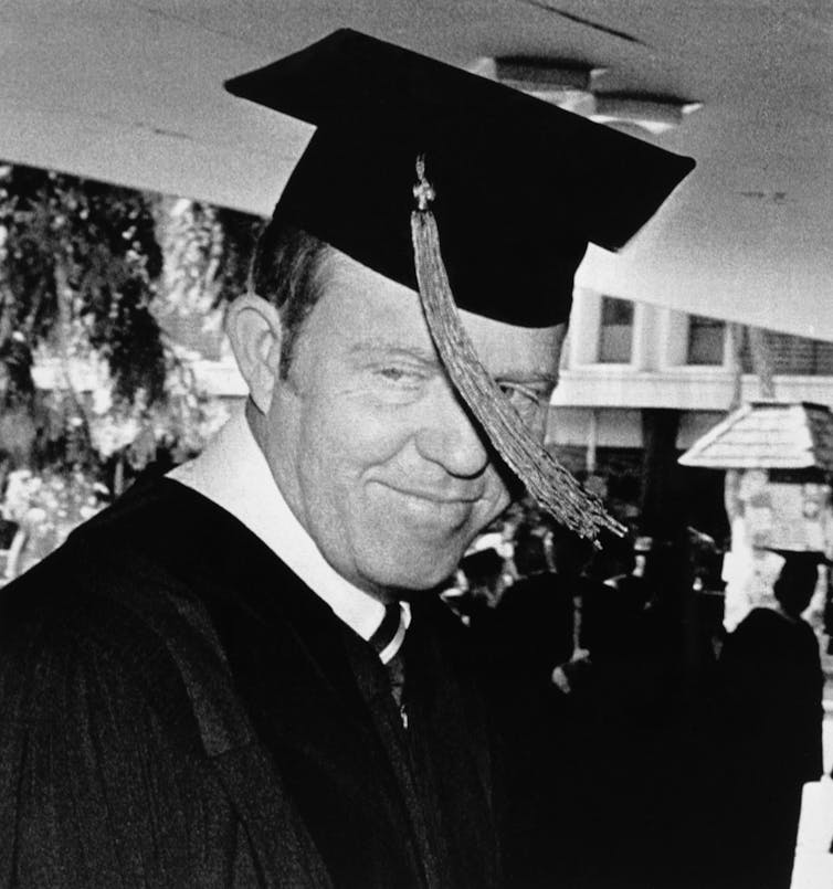 A white man wearing a black robe is seen graduating from medical school.