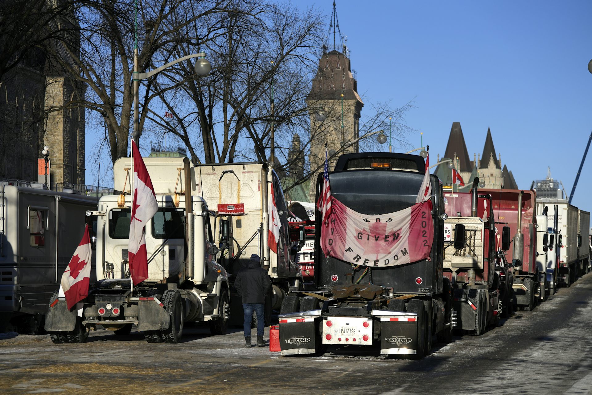Trucks are draped with Canadian flags along a busy Ottawa street with the Parliament buildings in the background.