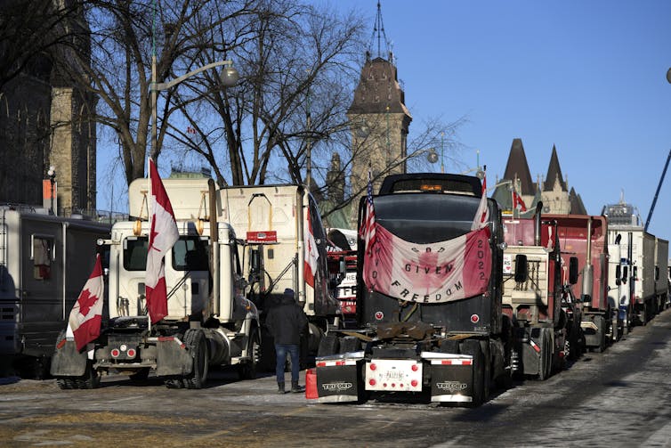 Trucks are draped with Canadian flags along a busy Ottawa street with the Parliament buildings in the background.