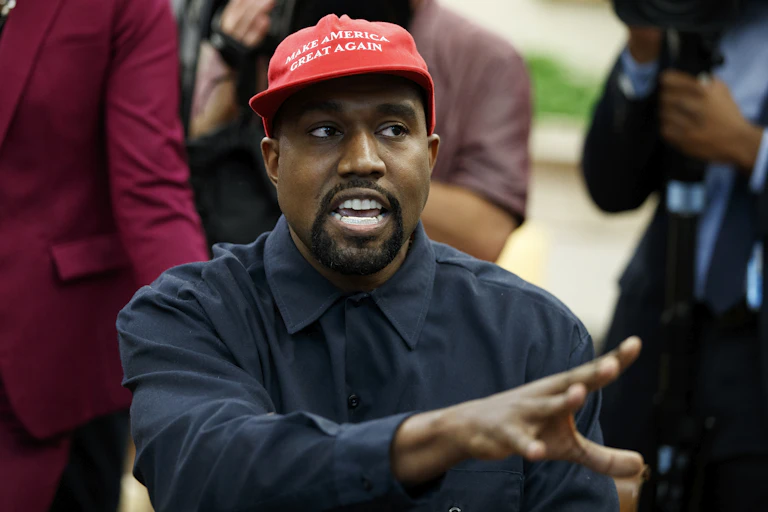a black man wearing a red make America great hat and a blue dress shirt gestures with his right hand