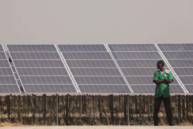 People stand next to solar panels of the solar energy power plant in Zaktubi, near Ouagadougou, on november 29, 2017