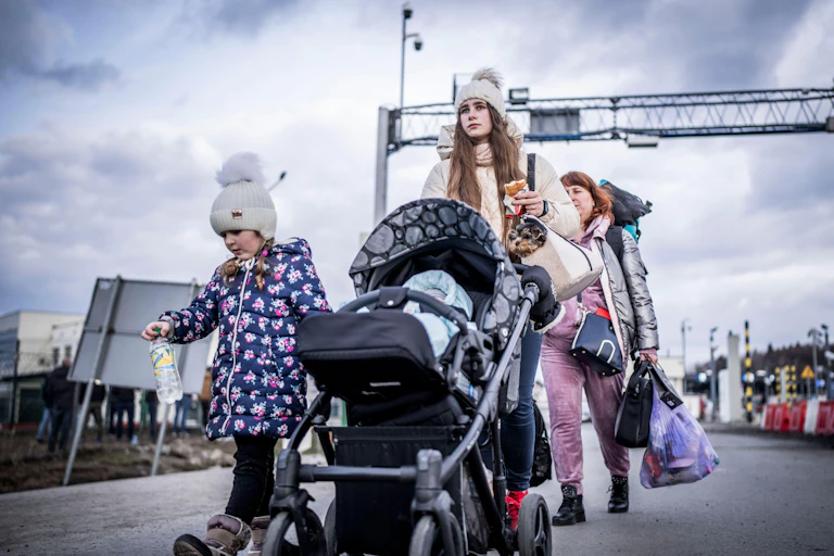 A Ukrainian woman with a baby in pushchair and another child walking beside her at the Polish border in February 2022.dren