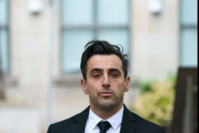 a man in a black suit and tie leaves a building