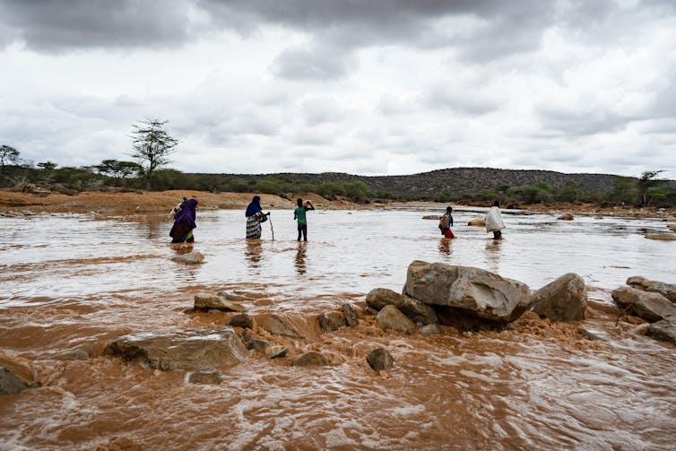 People stand in river, rainy sky.