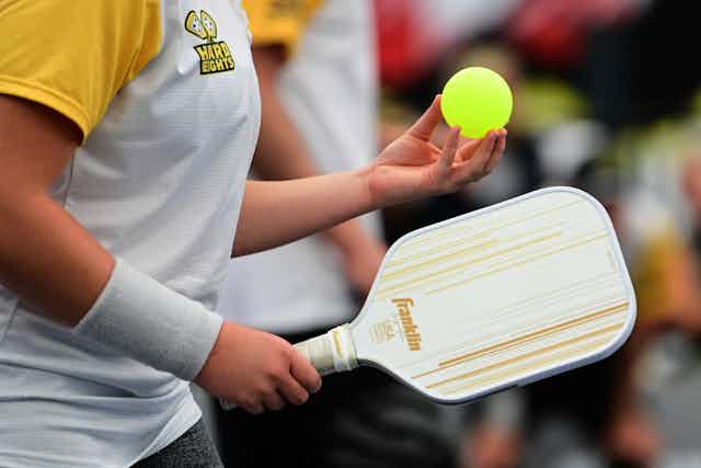 Closeup of pickleball player holding a racket and yellow ball.