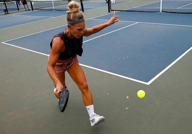 Female pickleball player lunges toward a ball to return a shot.