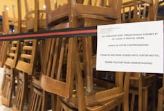 Stacked chairs are seen behind glass with a sign notifying people that a food court terrace is closed.