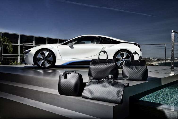 Four black luggage bags sit on the some black steps in front of a white luxury car
