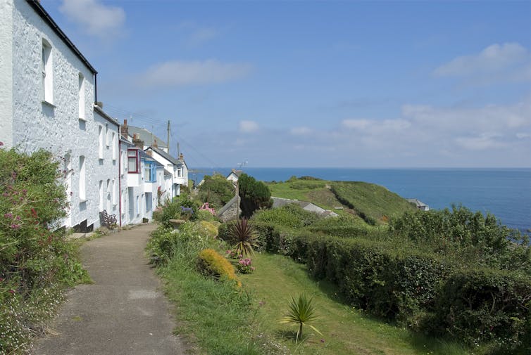 A row of white houses on top of a cliff overlooking the sea against a clear blue sky.