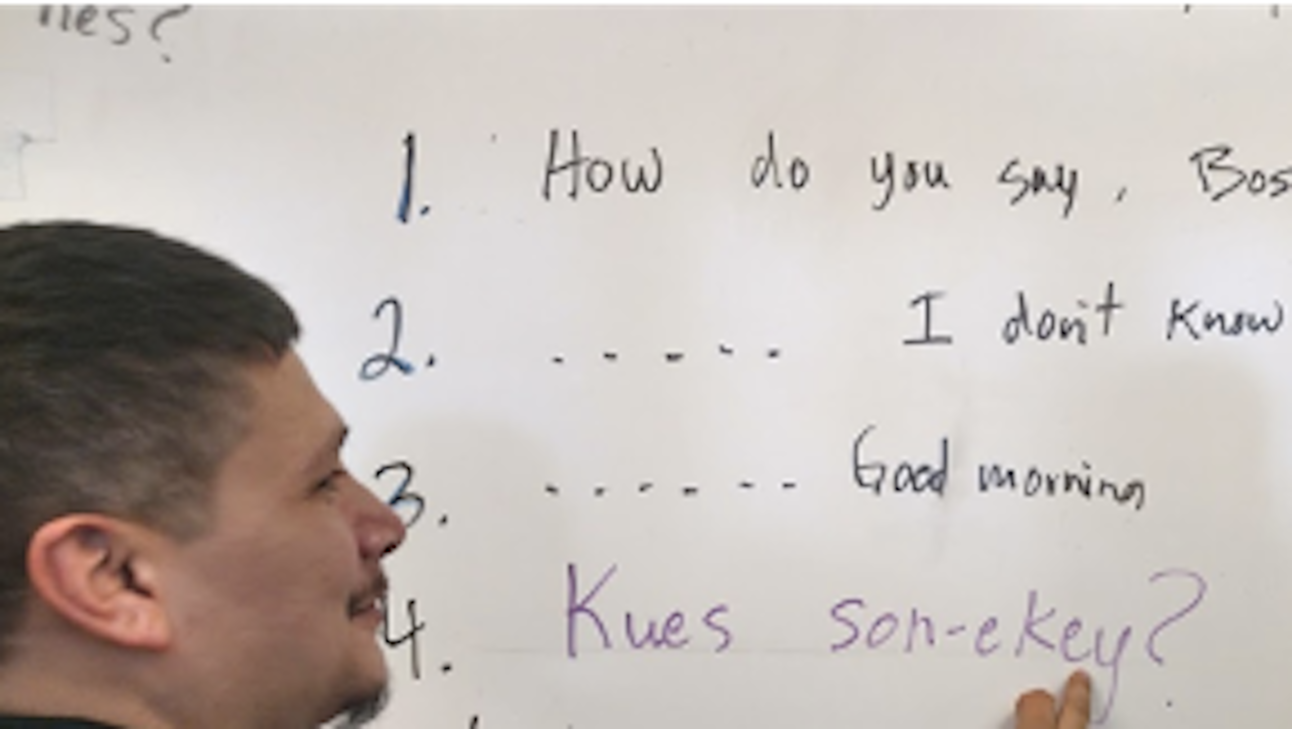 A teacher writes some words in an Indigenous language on a white board while a student looks.