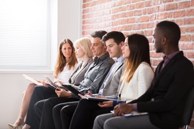 A row of people in business attire sitting on chairs, presumably waiting for an interview