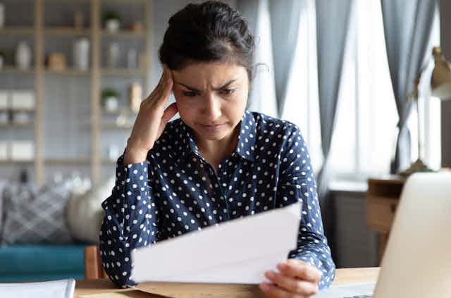 A confused-looking woman reads a piece of paper at a desk