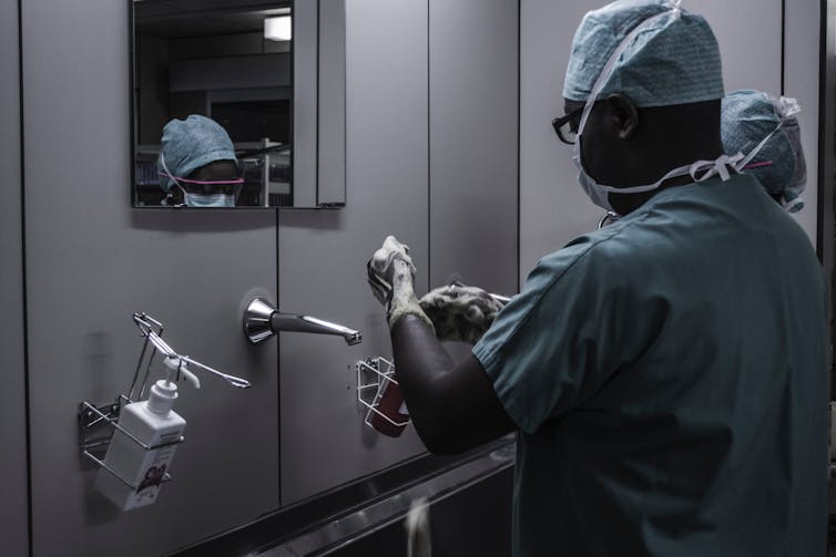 A Black medical professional adjusts gloves in front of a mirror.