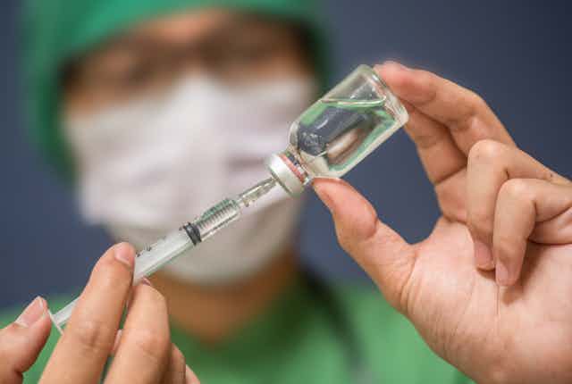 A person in a mask fills a syringe from a glass vial
