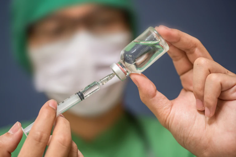 A person in a mask fills a syringe from a glass vial