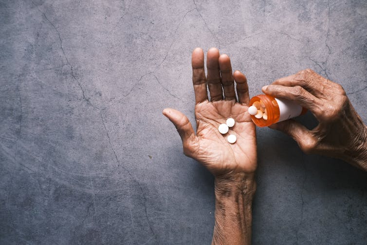 Una mano sostiene un frasco de pastillas y la otra mano sostiene tres pastillas blancas.