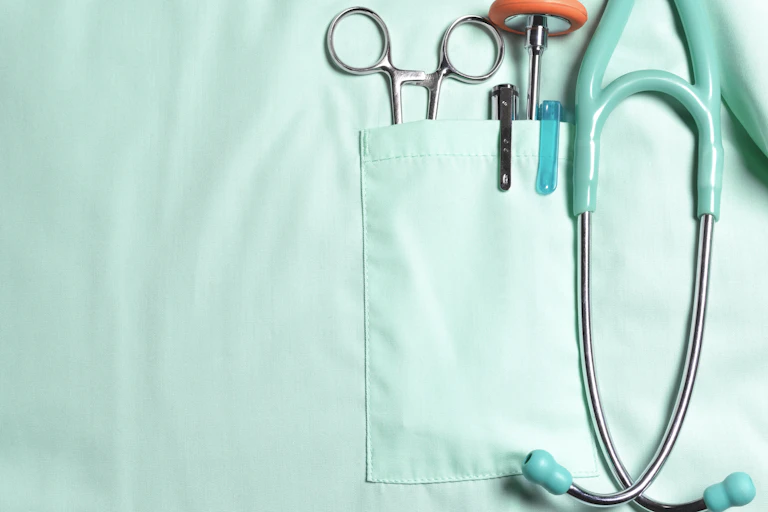 Close up of chest pocket of medical scrubs, holding stethoscope and other medical tools.