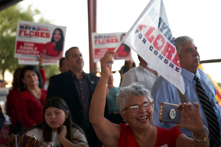 A group of people are waving campaign flags as they cheer for their political candidiates.