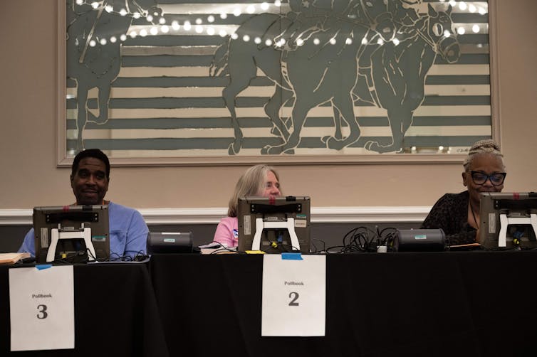 Three people sitting at computer screens at a table with a black tablecloth on it