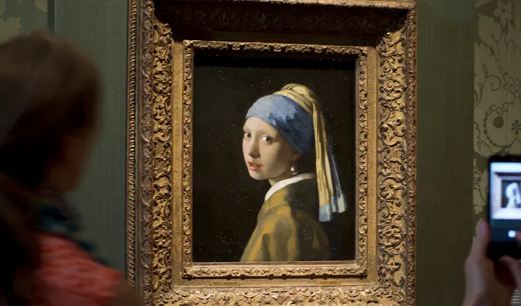 A gold-framed photo of a girl with a pearl earring against a green wall.