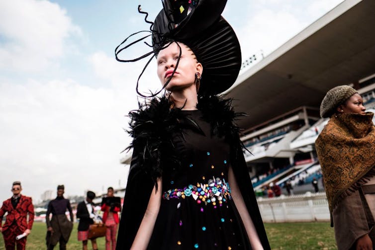 An albino fashion model wearing a black dress and black hat.