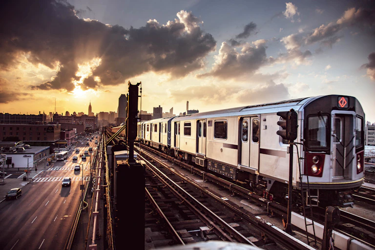 With a setting sun and a cloudy sky as a backdrop, an elevated subway car punctuates the New York City skyline.